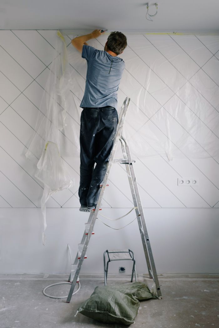 Full body back view of man in casual clothing plastering wall in empty room in daytime